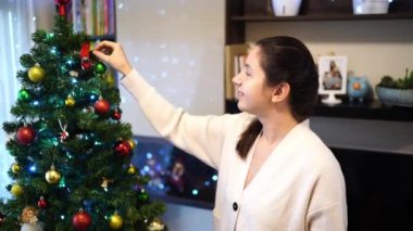 Genç, gülümseyen bir kadın Noel ağacına renkli toplar asıyor. Yüksek kalite 4k görüntü