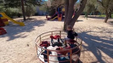 Küçük kız ağaçların arasında bir oyun parkında atlıkarıncaya biniyor. Yüksek kalite 4k görüntü