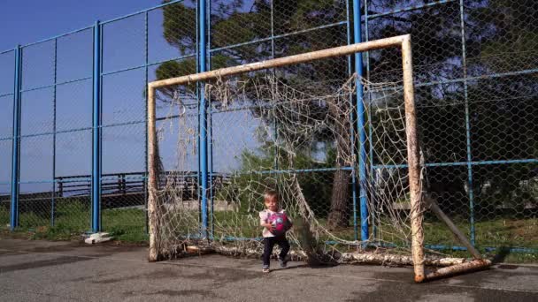 彼女の手に大きなボールを持つ小さな女の子は 遊び場のサッカーの目標から行きます 高品質4K映像 — ストック動画