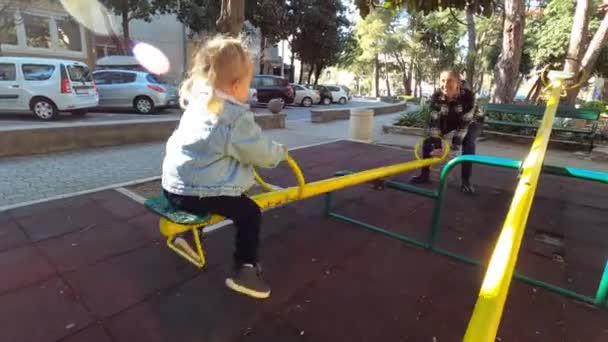 妈妈在房子院子里的操场上的秋千平衡器上摇动着一个小女孩 高质量的4K镜头 — 图库视频影像