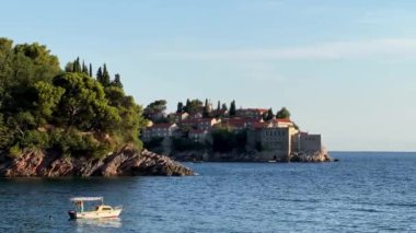 Sveti Stefan adası ve kayalık sahilin arka planında gezinti teknesi dalgalar üzerinde sallanıyor. Karadağ. Yüksek kalite 4k görüntü