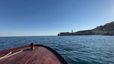 Mavi bir ufka karşı eski bir kasabanın sahil şeridine giden bir yelkenli teknesinin kıç tarafından görüntü. Yüksek kalite 4k görüntü