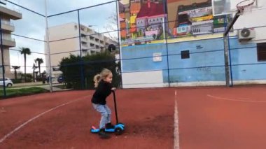 Küçük kız bahçedeki bir basketbol sahasında scooter kullanıyor. Yüksek kalite 4k görüntü