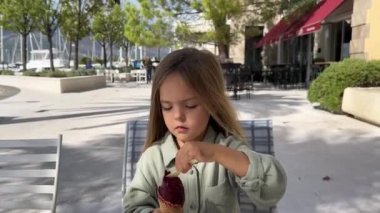 Küçük kız iskemlede otururken yanında spatulayla waffle külahında dondurma yiyor. Yüksek kalite 4k görüntü