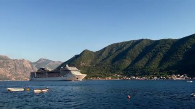 Dağ kıyısına yakın körfez boyunca büyük beyaz bir yolcu gemisi yelken açıyor. Yüksek kalite 4k görüntü