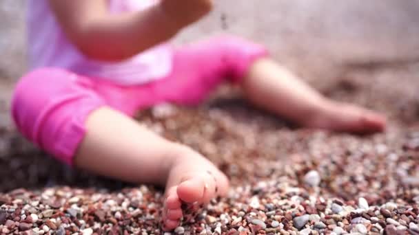 小女孩坐在一块石质的海滩上 把鹅卵石倒在地上 被收割了高质量的4K镜头 — 图库视频影像