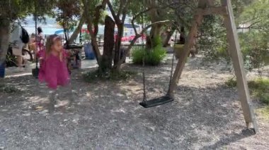 Küçük kız deniz kıyısındaki ağaçların arasında sallanıyor. Yüksek kalite 4k görüntü