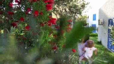 Anne, küçük kızını kollarında, çalıların üzerindeki kırmızı kalisiyum çiçeklerini gösteriyor. Yüksek kalite 4k görüntü