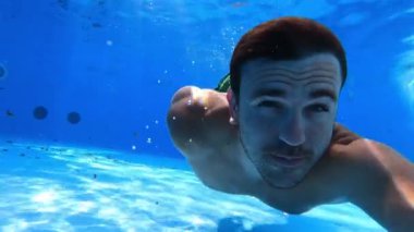 Gözleri açık genç adam havuzda suyun altında yüzer. Yüksek kalite 4k görüntü