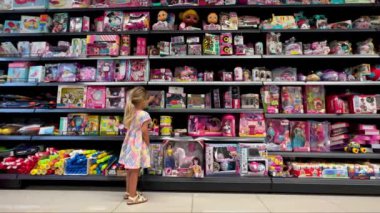 Küçük kız süpermarketin raflarının yanında yürüyor ve oyuncakları seçiyor. Yüksek kalite 4k görüntü
