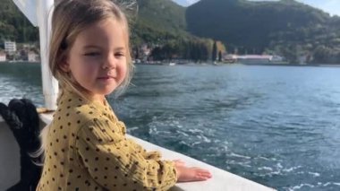 Küçük gülümseyen kız, dağların arka planına karşı denizde bir teknede yelken açıyor. Yüksek kalite 4k görüntü