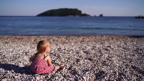 小女孩坐在卵石沙滩上 望着大海 高质量的4K镜头 — 图库视频影像