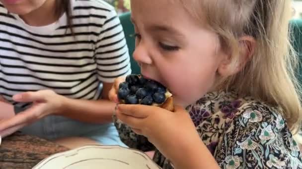 小女孩坐在她妈妈旁边的咖啡店里吃蓝莓蛋糕 高质量的4K镜头 — 图库视频影像