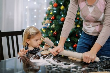 Küçük kız, annesinin masada merdaneyle hamuru yuvarlamasını izliyor. Yüksek kalite fotoğraf