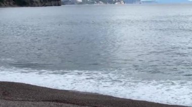 Deniz dalgaları bir dağ sırasının arka planında kumlu sahilde yuvarlanıyor. Yüksek kalite 4k görüntü