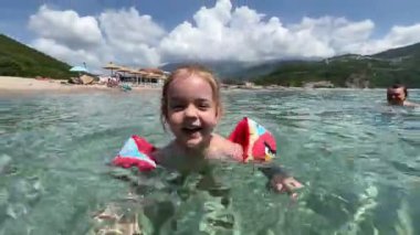 Küçük kız kollarında şişme kollarıyla denize su sıçratıyor. Yüksek kalite 4k görüntü