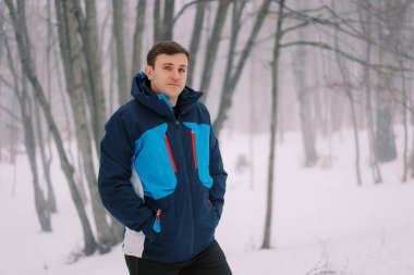 Elleri ceketinin cebinde gezgin karlı bir parkta bir ağacın yanında duruyor. Yüksek kalite fotoğraf