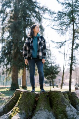 Genç bir kadın yosunla kaplı kocaman bir kütüğün üzerinde duruyor ve başka tarafa bakıyor. Yüksek kalite fotoğraf