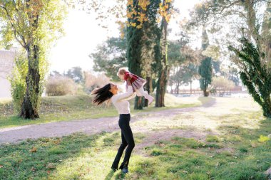 Annem sonbahar parkında küçük bir kızın kollarını çevirir. Yüksek kalite fotoğraf