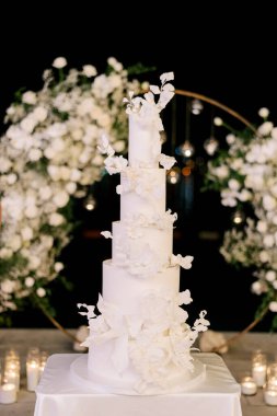 Çok katmanlı düğün pastası yuvarlak bir düğün kemerinin yanındaki masada duruyor. Yüksek kalite fotoğraf
