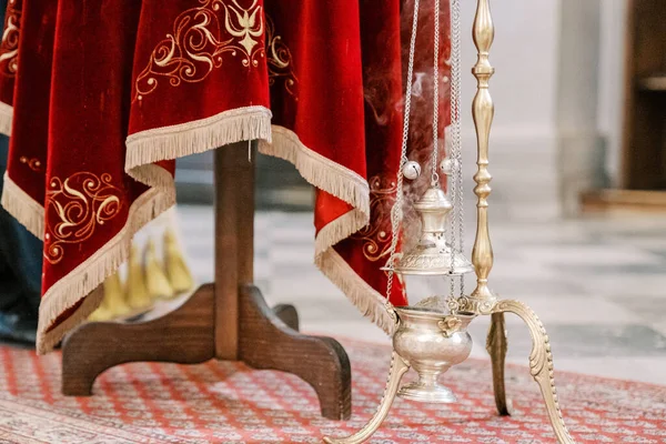 Smoking censer hangs on a gold chain on a stand near a table with a red tablecloth. High quality photo