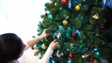 Genç bir kadın, çok renkli ışıldayan topların yanındaki Noel ağacına oyuncak asıyor. Yüksek kalite 4k görüntü