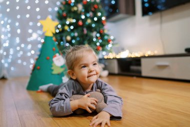 Minik gülümseyen kız, süslü bir Noel ağacının yanında oyuncak ayıya sarılıyor. Yüksek kalite fotoğraf