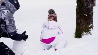 Annesiyle birlikte küçük bir kız ormanda kar altında bir kardan adam heykeli yapıyor. Yüksek kalite 4k görüntü