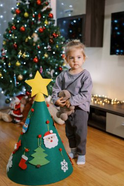 Küçük kız süslü bir Noel ağacının yanında oyuncak bir ayıyla duruyor. Yüksek kalite fotoğraf