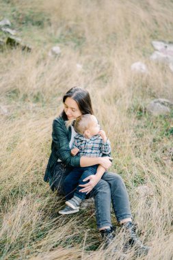 Annem küçük bir kızı kollarında, gözleri kapalı çimenlerde otururken kucaklıyor. Yüksek kalite fotoğraf