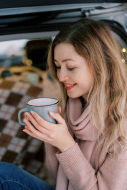 Battaniyenin üzerinde otururken elinde kahve fincanına bakan gülümseyen genç bir kadın. Yüksek kalite fotoğraf