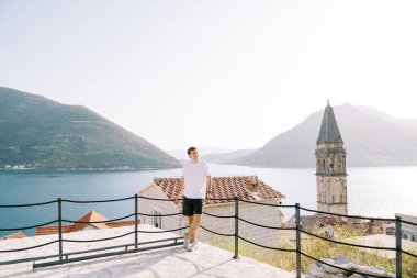 Gülümseyen adam kilisenin çan kulesinin yakınındaki bir gözlem güvertesinde çitlere yaslanıyor. Perast, Karadağ. Yüksek kalite fotoğraf