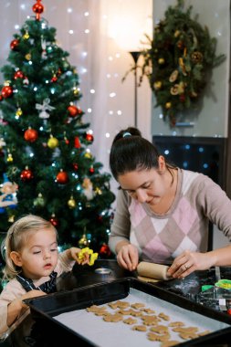 Annesi hamuru merdaneyle sararken küçük kız da tepsideki kurabiyelere bakıyor. Yüksek kalite fotoğraf