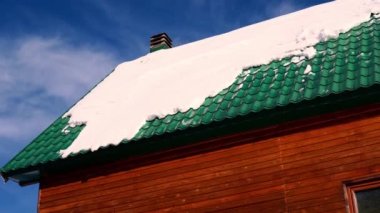 Kar, güneşin altındaki ahşap bir evin yeşil kiremitli çatısında yatar. Yüksek kalite 4k görüntü