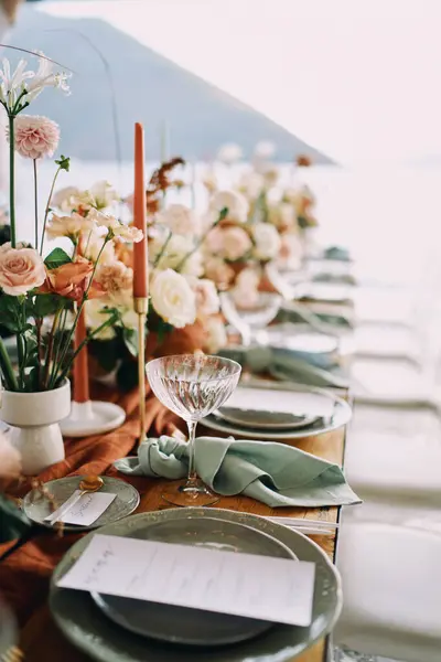 Knotted napkins lie next to a plate with a festive menu and bouquets of flowers on a table by the sea. High quality photo