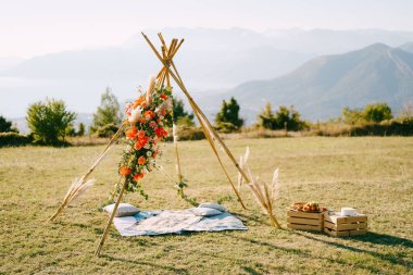 Tipi tarzı düğün kemeri dağlardaki yeşil bir çayırda tahta kutuların yanında duruyor. Yüksek kalite fotoğraf