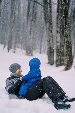 Karda sırt üstü yatan gülümseyen anne karnında küçük bir çocuk oturuyor. Yüksek kalite fotoğraf