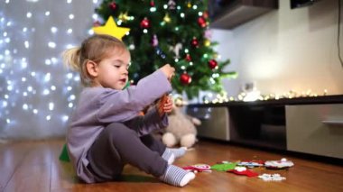 Küçük kız yerde duran keçeli oyuncaklarla Noel ağacını süslüyor. Yüksek kalite 4k görüntü
