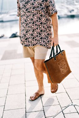 Sahil çantalı şortlu bir adam bahçedeki fayanslarda yürüyor. Kırpılmış. Yüzsüz. Yüksek kalite fotoğraf