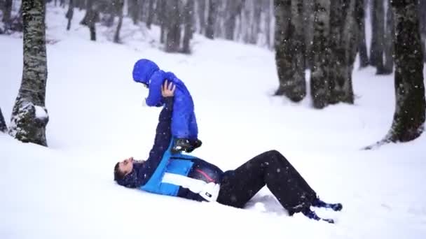 父親は雪の下で雪の中に横たわっている彼の腕の中で小さな子供を育てます 高品質の4K映像 — ストック動画
