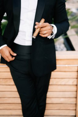 Elinde puroyla damat, tahta bir saksıya yaslanmış duruyor. Kırpılmış. Yüzsüz. Yüksek kalite fotoğraf