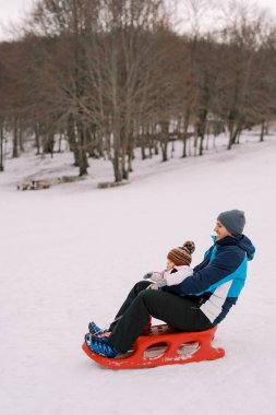 Kollarında küçük bir çocukla gülümseyen baba dağdan aşağıya kızakla iniyor. Yan görüş. Yüksek kalite fotoğraf
