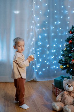 Küçük kız elinde bir topla süslü bir Noel ağacının yanında duruyor. Yüksek kalite fotoğraf