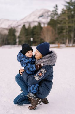 Annem karlı bir çimenlikte çömelirken kucağındaki küçük çocuğa bakar. Yüksek kalite fotoğraf