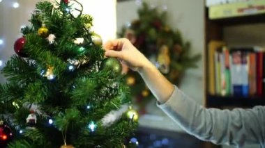 Kadın eli, odadaki bir Noel ağacının dalına parlak bir top asıyor. Yüksek kalite 4k görüntü