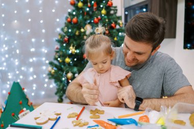 Küçük kız babasının kucağına oturur ve Noel kurabiyelerini parlatırken onu izler. Yüksek kalite fotoğraf