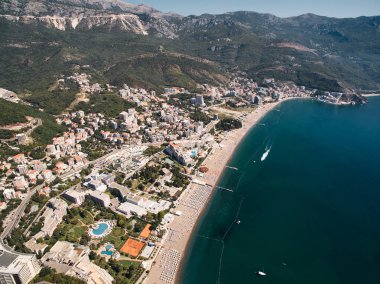 Deniz kıyısında güneş şemsiyeli Budva kıyıları ve dağların eteğindeki modern oteller. Karadağ. Drone. Yüksek kalite fotoğraf