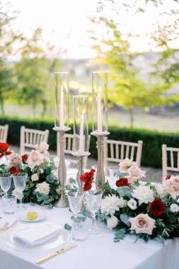 Cam kapaklı şamdanlarda parlayan mumlar çiçeklerin arasında bir şenlik masasında duruyor. Yüksek kalite fotoğraf