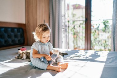 Küçük kız yatağa oturur ve yalancı bir kedinin yanında oyuncak tarar. Yüksek kalite fotoğraf