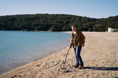 Plaj polisi kumda yürürken metal dedektörü araklıyor. Yüksek kalite fotoğraf
